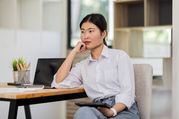 Obraz premium Young modern business asian woman working using digital tablet while sitting in the workplace office
