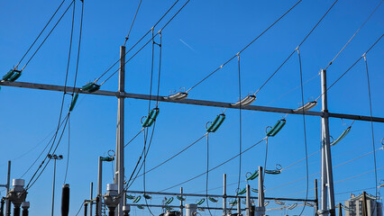 High voltage electrical insulators in power transmission substation against blue sky background;...