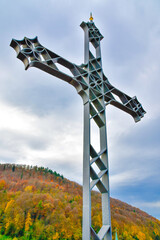 An imposing large metal cross stands majestically in front of a mountain