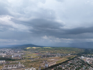Mountain landscape in summer before the rain. The sun rays break through the clouds. City near the mountains. Top view, drone photo. © Anton