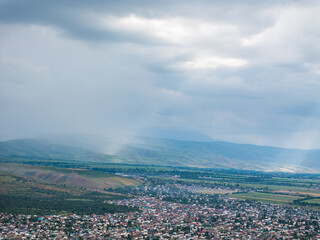 Obraz premium Mountain landscape in summer before the rain. The sun rays break through the clouds. Village near the mountains. Top view, drone photo.