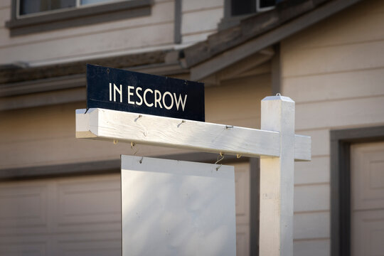 A sign stating In Escrow with a house in the background