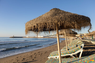 Close-up of a parasol and sunbeds in La Carihuela and Benalmádena in the background.