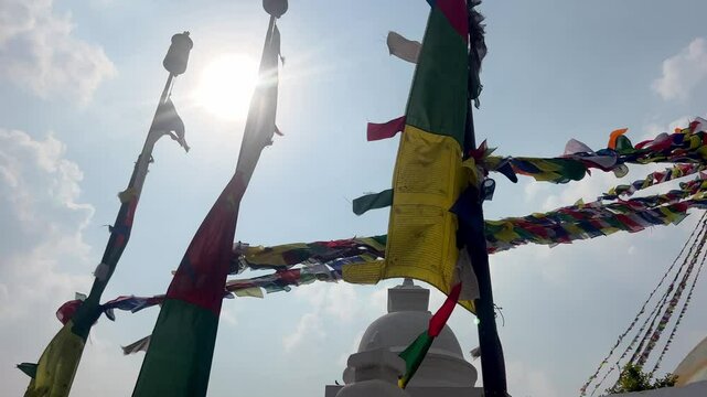 Tibet prayer flag attached on poles are waving in the foreground. in the background the top of a Buddhist temple