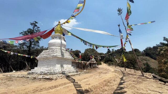 A Buddhist stupa in the nature on a trekking path. Little temple with a golden dome, the buddha's eyes on top and the traditional colourful prayer flags that waving