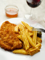 Breaded chicken fillet meal and fried potatoes chips with ridges on a white plate and light color table cloth. Simple food made of high quality premium products. Cooked poultry meat.