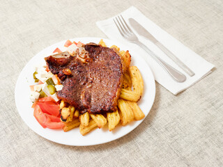 Dinner with premium t bone steak, fried potatoes chips with ridge, fresh salad with feta cheese on white plate and light color table cloth. Large portion of food with high quality products.