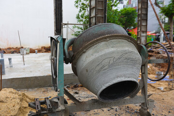 Rusty concrete mixer at construction site with unfinished foundation