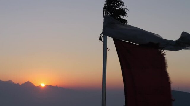 Silhouette of Tibetan prayer flags that waving on the top of a pole. In the background the sunrise on the Himalayan range