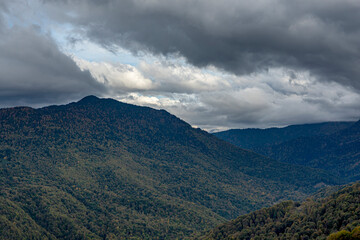 Fototapeta premium Cloudy evening at a picturesque mountain resort in autumn, heavy thunderclouds. Mountain peaks are shrouded in dark clouds. Early autumn, picturesque mountain ranges