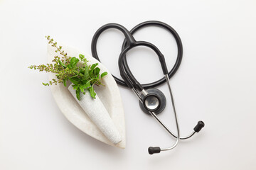 Close-up of fresh organic green Holy Basil or Rama Tulsi (Ocimum sanctum) leaves leaves, placed on a white marble mortar and pestle with stethoscope, isolated on a white background.