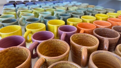 Obraz premium A beautifully arranged collection of handmade ceramic mugs showcasing a spectrum of vibrant colors. The mugs, crafted with textured and speckled finishes, are neatly aligned on a white surface.
