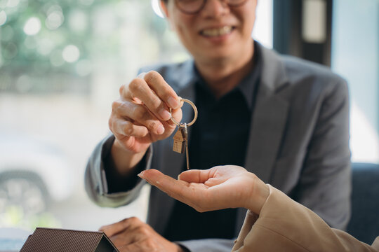 Handing Over Keys to New Home: A smiling real estate agent presents keys to a happy new homeowner, symbolizing a successful real estate transaction and the beginning of a new chapter. - Powered by Adobe