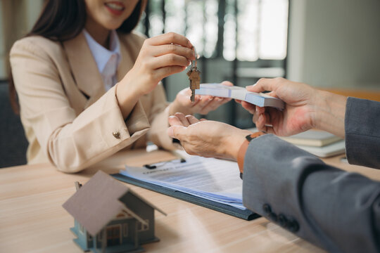 Real Estate Transaction: Agent handing over keys and receiving payment from a buyer at a closing table.  A successful property deal is finalized. 