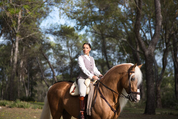 portrait of equestrian woman, young and beautiful, riding and holding the reins of her purebred...