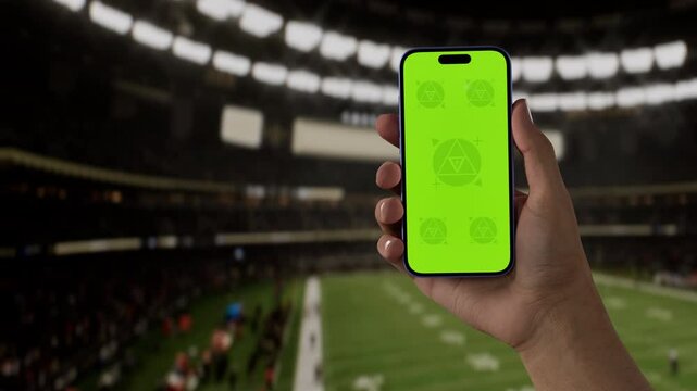 GREEN SCREEN CHROMA KEY A hand holding a phone with a green screen at an American football game in a stadium at night, perfect for showcasing live sports or betting apps - Powered by Adobe