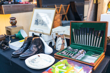Antique flea market. Leather shoes, painting, set of tableware, vase, and plates for sale