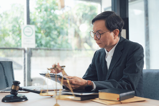 Focused Lawyer Reviewing Documents: A meticulous lawyer, wearing glasses and a dark suit, intently reviews legal documents at his desk.
