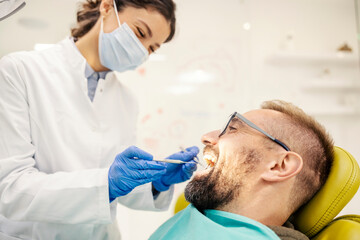 Patient sitting in chair with mouth open while dentist examining his teeth at dentist office.