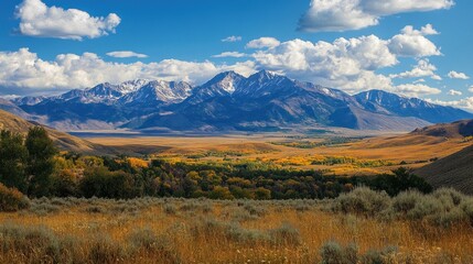 Fototapeta premium Scenic autumn valley with golden grasses and snow-capped mountains under a blue sky.