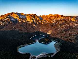 aerial view of black lake with pine forest and mountain range during sunrise