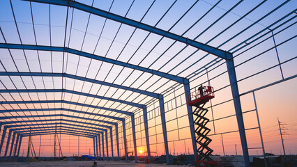 Silhouette factory building framework with welder worker on electric scaffolding working overtime...