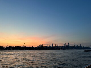 Fototapeta premium Serene sunset view across the water with the iconic New York City skyline silhouetted against colorful evening sky.