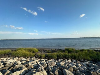 Scenic view of calm waters meeting rocky shore, framed by green grass and blue skies, ideal for nature-related projects and serene backgrounds.