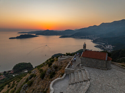 aerial view on sveti stefan chutch on top of mountain with budva, bay and mountains one the background during sunset