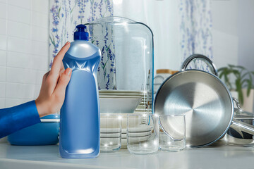 Unbranded dishwashing detergent in front of spotlessly clean dishes and a hand holding a detergent box. Advertisement in the kitchen, in front of the sink and clean dishes