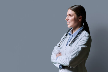 Profile view of young positive female doctor with stethoscope on gray background