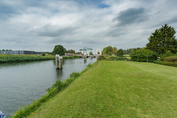 Obraz premium Scenic view of a tranquil canal surrounded by lush greenery and cloudy skies in a rural area