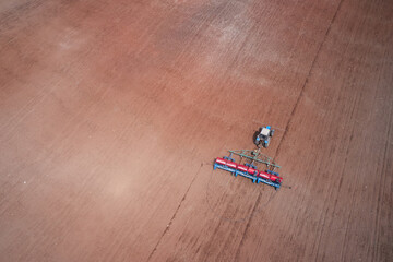 Sowing company. Tractor with trailed grain seeder sows wheat seeds into red soil. Shooting from a...