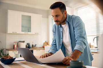 Male entrepreneur using laptop while working on business reports at home.