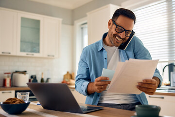Happy entrepreneur talking on cell phone while analyzing business reports at home.