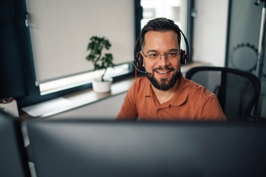 Smiling male call center agent working on computer in office