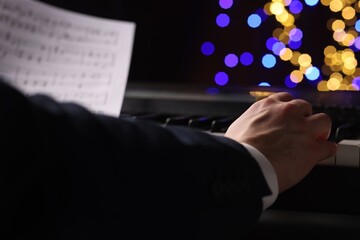 Man playing piano against blurred lights, closeup. Bokeh effect