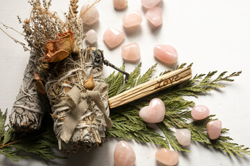 A close up image of three white sage smudge sticks with small polished rose quartz crystals. 