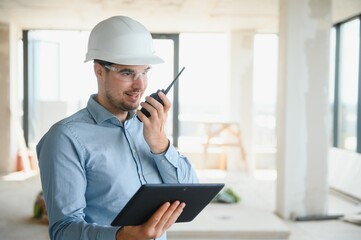 Supervisor standing in building in construction process, holding tablet and checking on works