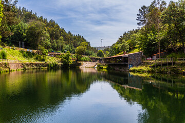 Obraz premium A tranquil lake surrounded by lush green forests, with a small building on the shore and a bridge crossing the water