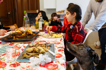 dog sitting next to the festive table waiting for the food while children are eating