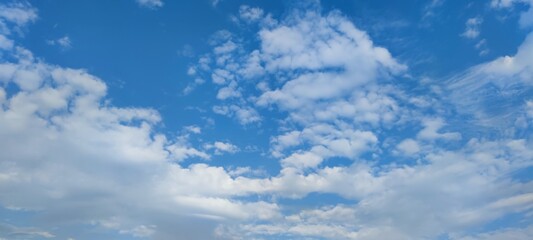 Obraz premium Clouds at different levels. Bright summer sky. High, semi-transparent cirrus clouds and low cumulus clouds spread across the sky. Clouds of gray and white colors of different shapes and sizes.
