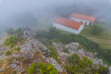 A misty, atmospheric view of a rocky clifftop, with a hint of a building or structure shrouded in...