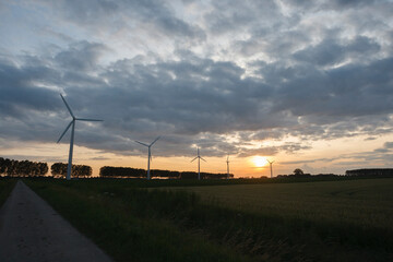 Obraz premium Wind turbines under a dramatic sunset sky in a rural landscape showcasing renewable energy