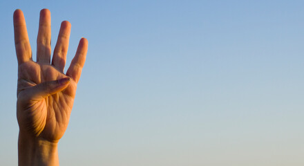 Hand showing number four gesture on blue sea sky background. Gesturing number 4 index finger. Making number four in sign language. Hand counting four. Space for ad text