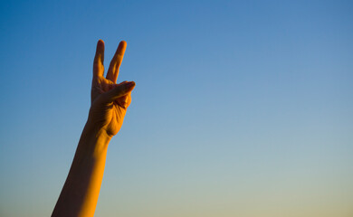 Hand showing number two gesture on blue sea sky background. Gesturing number 2 index finger. Making number two in sign language. Hand counting two. Space for ad text
