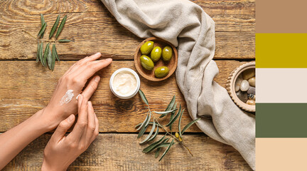 Woman applying natural olive cream onto her hand on wooden background