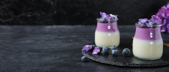 Glasses of panna cotta with blueberry and beautiful hydrangea flowers on black table