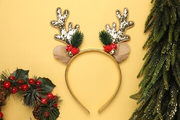 Beautiful reindeer headband and Christmas decor on pale yellow background, flat lay