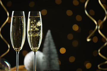 Delicious champagne in glasses and Christmas decor against black background with blurred lights, closeup. Space for text